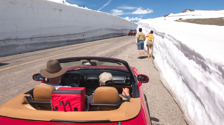 A car with the top down parked on the side of the road where snow has piled up over 6 feet