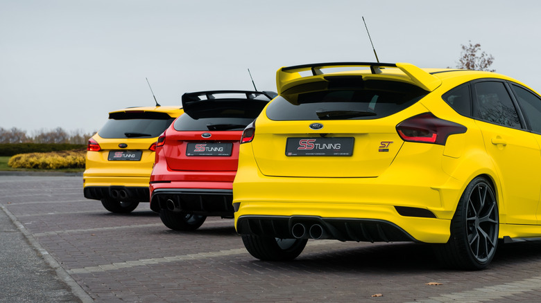 Rears of two yellow Focus ST and one red Focus RS parked in empty parking lot. Rear three quarter view of three Ford hatchbacks. Kharkiv, Ukraine - November 05 2017