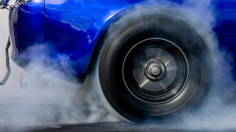 A drag racing car's rear wheel doing a burnout and creating smoke