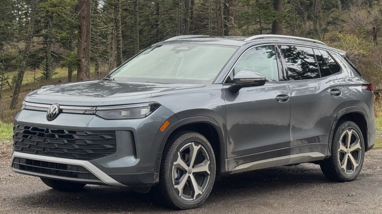 front three-quarters shot of a dark gray Volkswagen Tiguan parked on dirt in front of trees