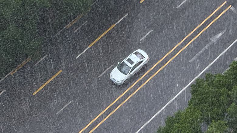 CHONGQING, CHINA - JUNE 19: A white car drives alone on a nearly empty city road during a heavy rainstorm near a pedestrian crosswalk on June 19, 2025 in Chongqing, China. The intense rainfall reflects typical summer monsoon conditions, contributing to low visibility and wet driving surfaces across the urban landscape. (Photo by Cheng Xin/Getty Images)