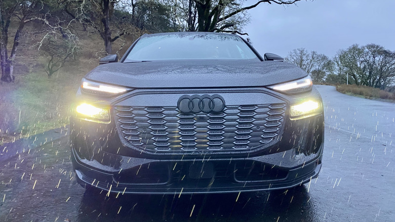 head-on shot of a dark gray Audi SQ6 E-Tron with its headlights on while parked on a road in the rain at dusk