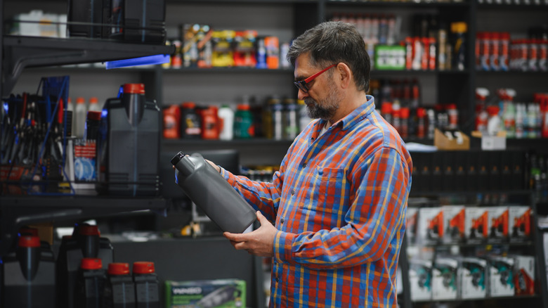 Mature customer selecting motor oil in an auto parts store, intently reading the label on a bottle while considering options for vehicle maintenance