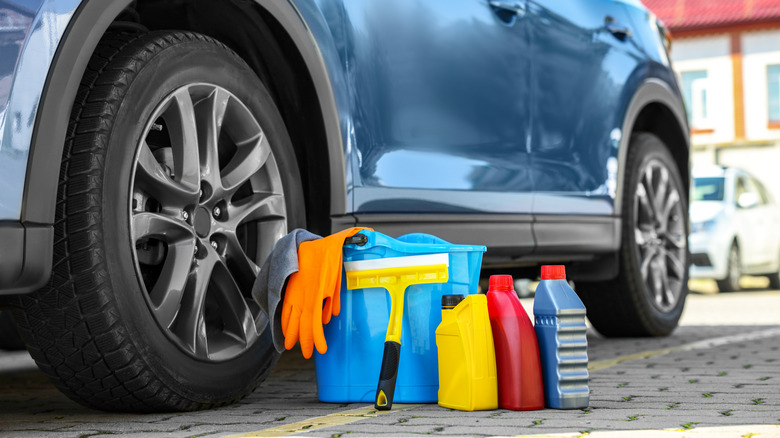 Car cleaning products and bucket near automobile outdoors on sunny day