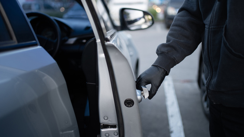 Close-up shot of a thief wearing a black shirt and black gloves. He tried to open the car door and tried to break in.