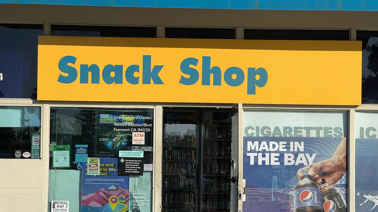 Facade of a gas station snack shop with large yellow and blue signage and various advertisements in the windows, Mission Boulevard, Fremont, California, August 31, 2024.