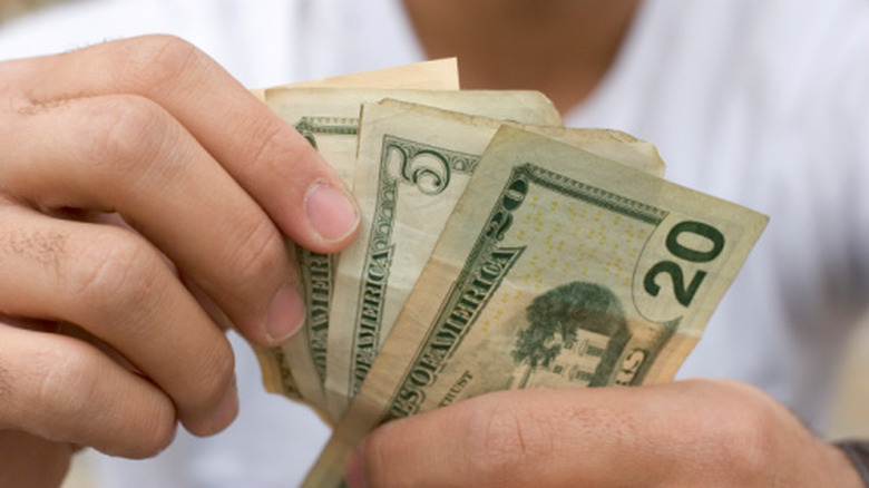 A person holding several U.S. dollar bills, including a $20 bill.