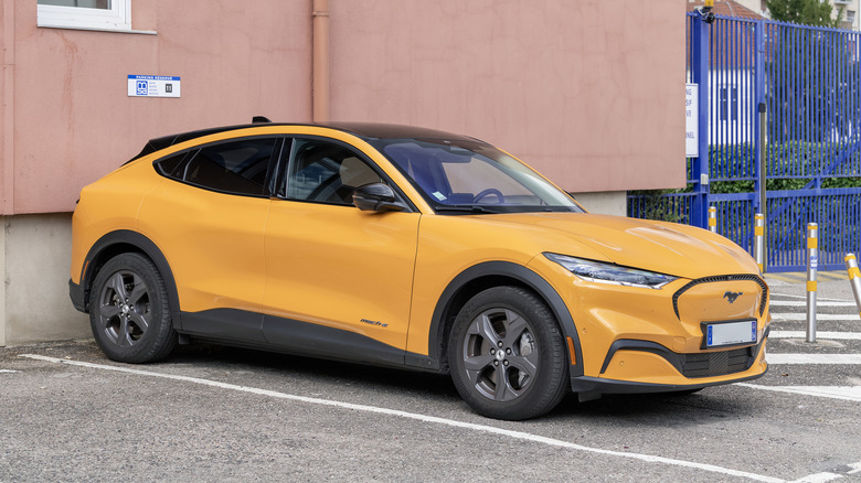 An orange Mustang Mach-E parking outside of a building