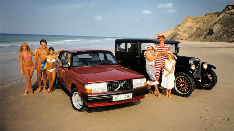 People posing on the beach in front of two old Volvos