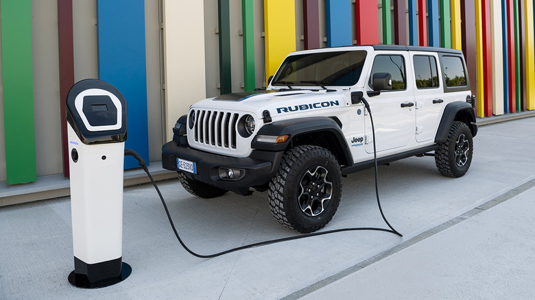 A white Jeep Wrangler 4xe parked on concrete next to a wall of colorful vertical lines while plugged in to an EV charger