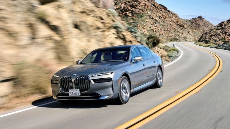 A front three quarters shot of a silver BMW i7 driving on a mountain road past rocky brown mountains
