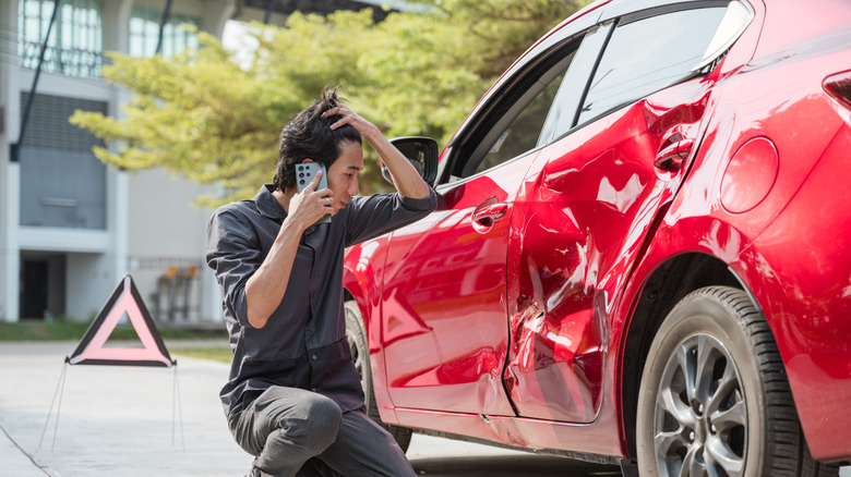 Car accident crash, Car accident protection, Claim collision, Auto emergency. Crashed car claim insurance. A man is kneeling down next to a red car that has been in an accident.