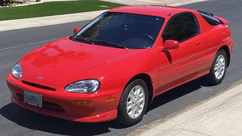 Front three quarters shot of a bright red Mazda MX-3 V6 parked on the streetin front of grass
