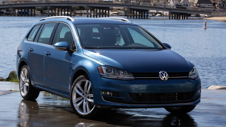 A blue volkswagen sportwagen parked next to water, with a bridge in the background