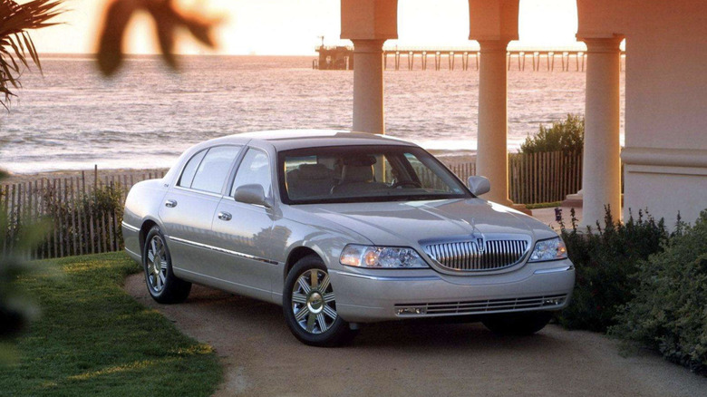 A Lincoln Town Car parked in front of the ocean with a large dock in the background