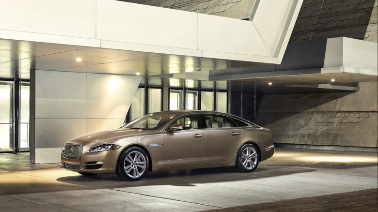 A gold Jaguar XJ parked in front of a modernist building