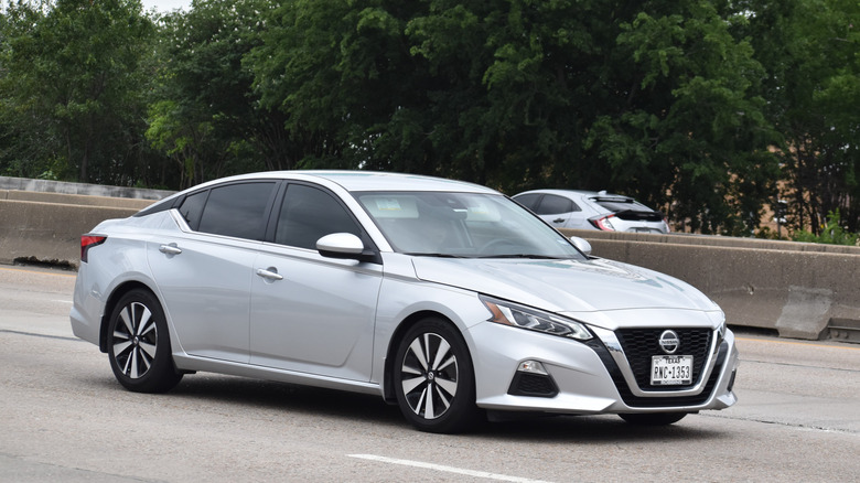 A portrait of a Nissan Altima traveling down a highway in moderate traffic