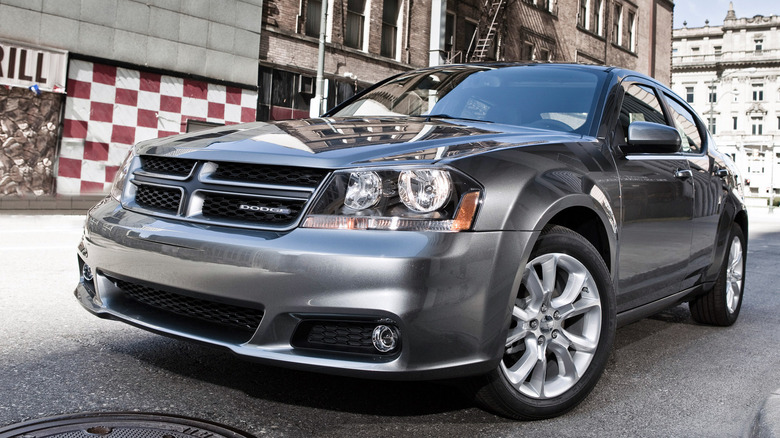A gray Dodge Avenger sedan parked with a city background