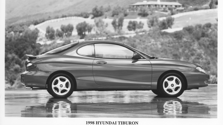 A achromatic and achromatic broadside position of nan first-generation Hyundai Tiburon parked connected bedewed crushed successful beforehand of hills