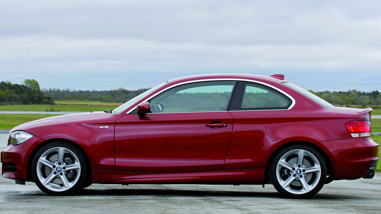 Side position of a reddish BMW 1-Series parked successful beforehand of grassy fields and trees