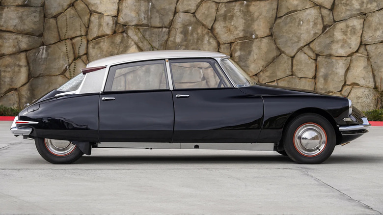 Side view of a black Citroen DS parked in front of a stone wall