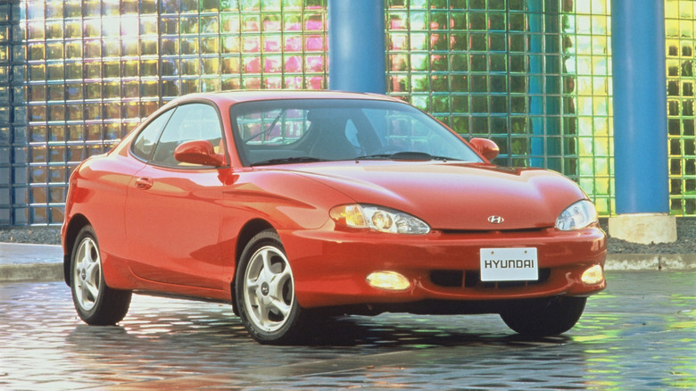 front 3 quarters changeable of a reddish Hyundai Tiburon parked successful beforehand of a wall of solid bricks