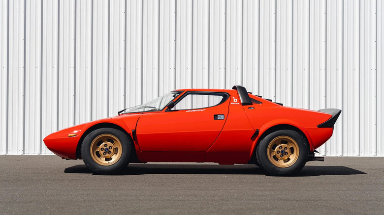 Side view of a red Lancia Stratos HF parked in front of a corrugated steel white wall