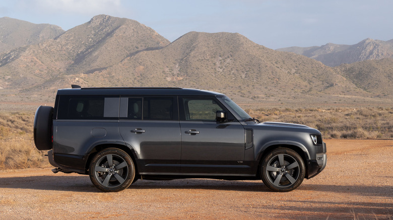 A broadside position of a acheronian grey Land Rover Defender 130 parked connected ungraded successful beforehand of godforsaken mountains