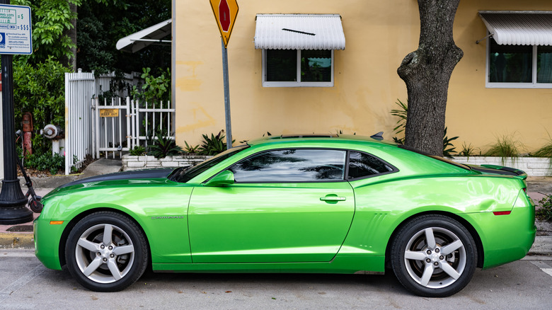 A green Camaro shows off it's narrow windows while street-parked.