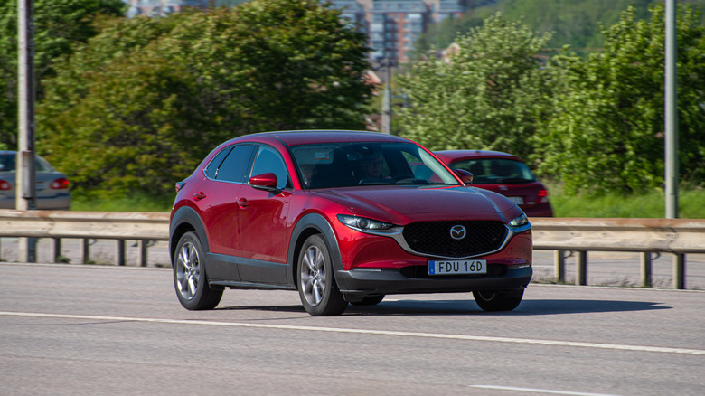 A red Mazda CX-30 drives on the road.