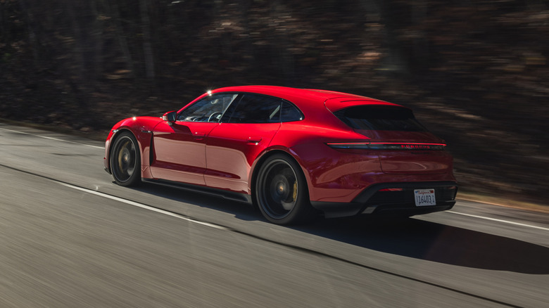 rear three-quarters shot of a red Porsche Taycan Sport Turismo driving past dark trees