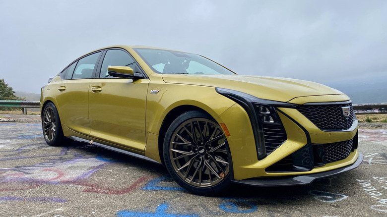 front three-quarters shot of a yellow Cadillac CT5-V Blackwing parked on graffiti-covered asphalt in front of a gray cloudy sky