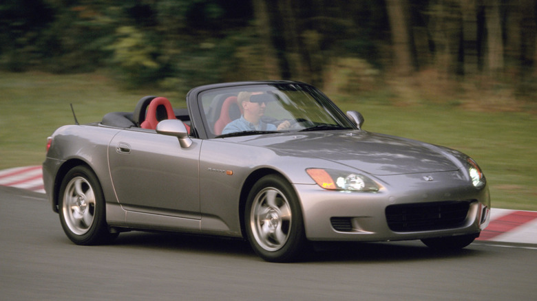 front three-quarters shot of a silver Honda S2000 driving around a corner on a race track past grass and trees