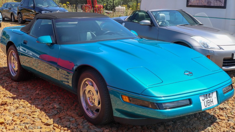 A blue 1992 Chevy Corvette parked in a gravel lot with other cars in the background