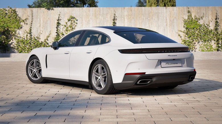 rear three-quarters shot of a white base Panamera parked on gray brick in front of a light colored wall with green plants growing up it