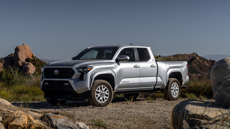 Front three quarters shot of a silver Toyota Tacoma parked on gravel around rocky peaks