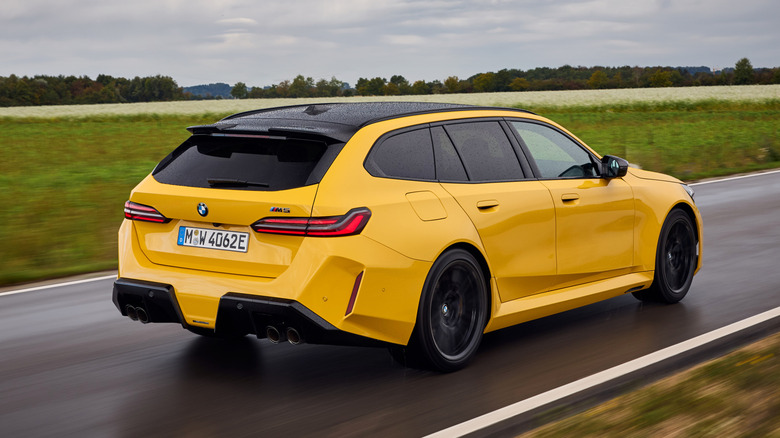 Rear 3/4 view of a yellow BMW M5 Touring driving next to a field