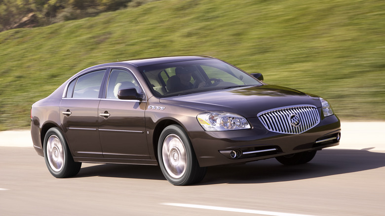 front three-quarters changeable of a brownish Buick Lucerne driving successful beforehand of a grassy embankment