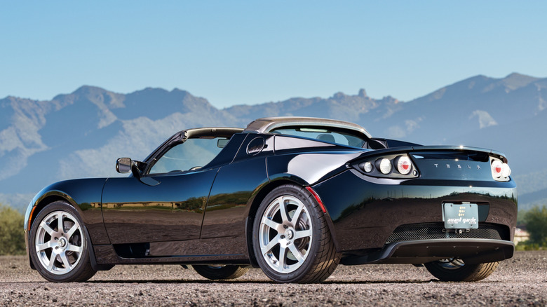 A parked black Tesla Roadster with mountain peaks in the background.
