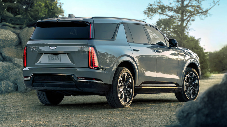 rear three-quarters shot of a gray Escalade IQ parked outdoors on dirt in front of rocks and trees