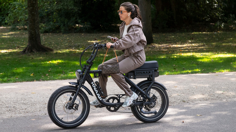 Amsterdam, Netherlands, September 7, 2025; Young woman with earphones on and cell phone in her hand on a fatbike in the Vondelpark in Amsterdam.
