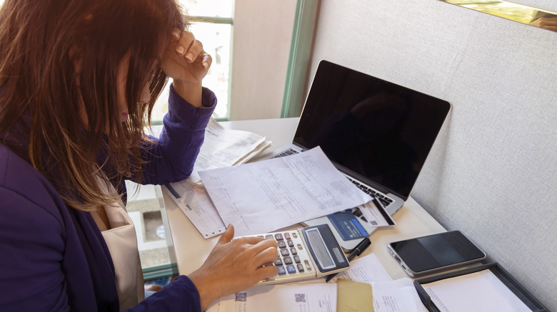 A woman with a calculator, stressed out by bills on her desk