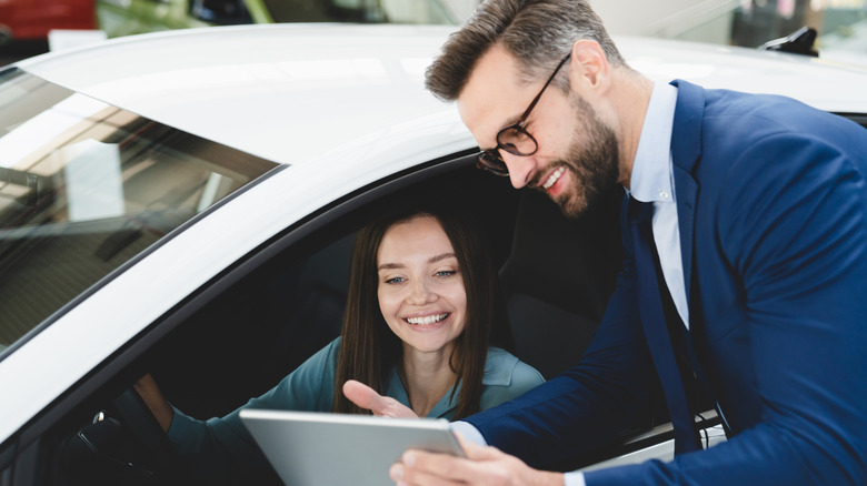 Car salesman hands a smiling woman a clipboard