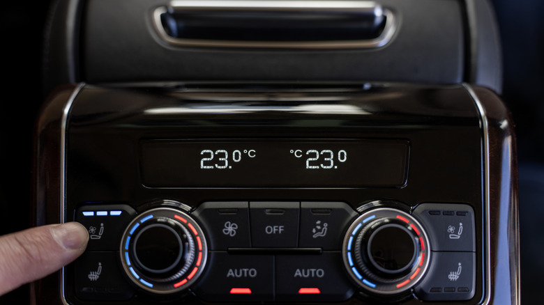 Passenger adjusting seat ventilation and climate control temperature on the rear seat climate control panel in a luxury car.
