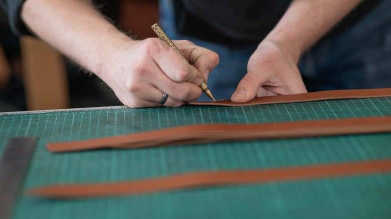 Leatherworker measuring and cutting leather in workshop.