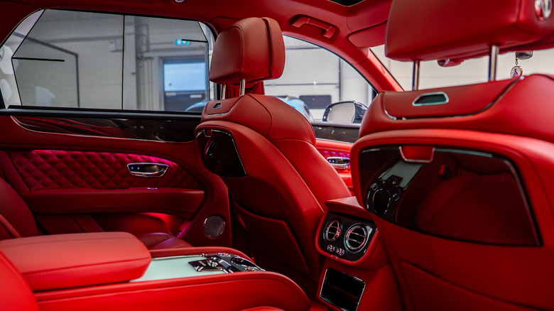 Luxurious red leather interior of a Bentley Bentayga with quilted patterns, polished wood trim, chrome accents, and advanced control panels in a showroom.