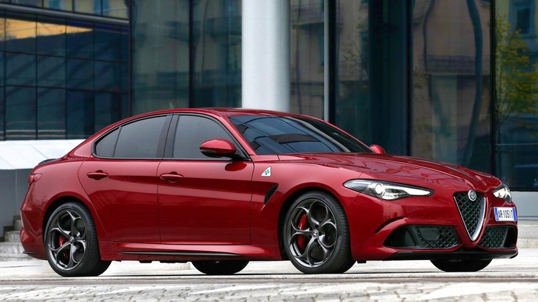 Side shot of a red Alfa Giulia Quadrifoglio parked on a street in front of a glass building