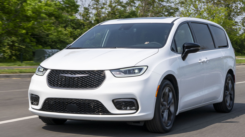 Front three quarters shot of a white Chrysler Pacifica driving on a road past grass and trees