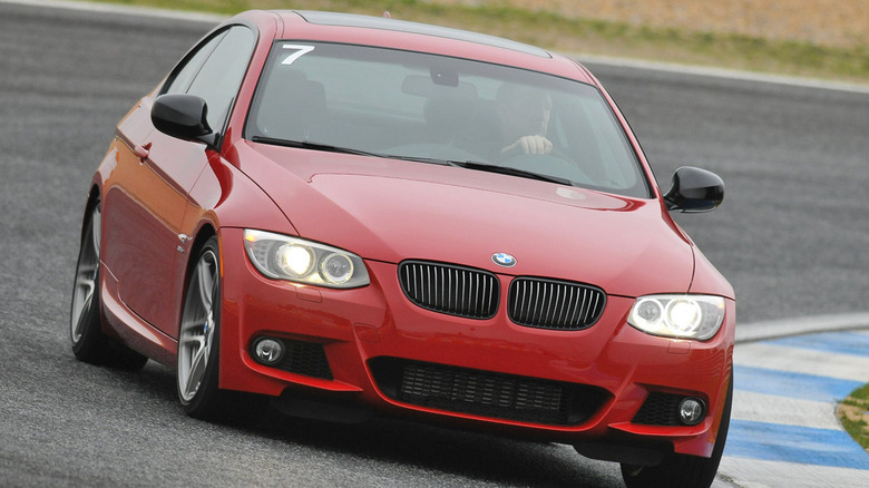 Head-on shot of a red BMW 335is driving around a corner on a race track with a number 7 on the windshield