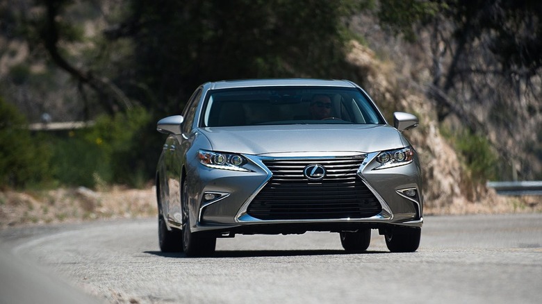 A head-on shot of a silver ES350 driving on a mountain road with a blurry mountain face behind it